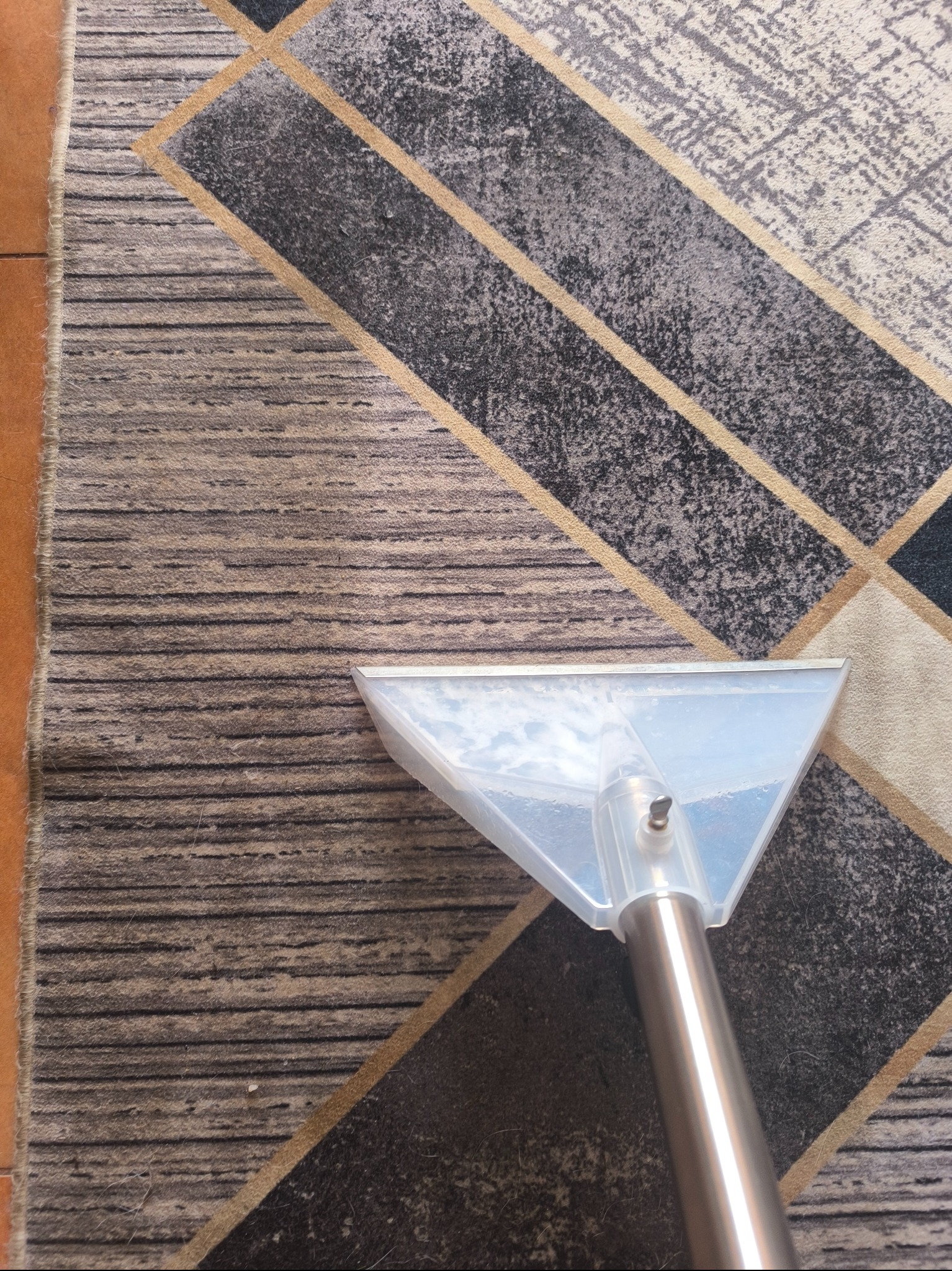 Czyszczenie wzorzystego dywanu metodą ekstrakcyjną z użyciem przezroczystej dyszy z metalową rurą.