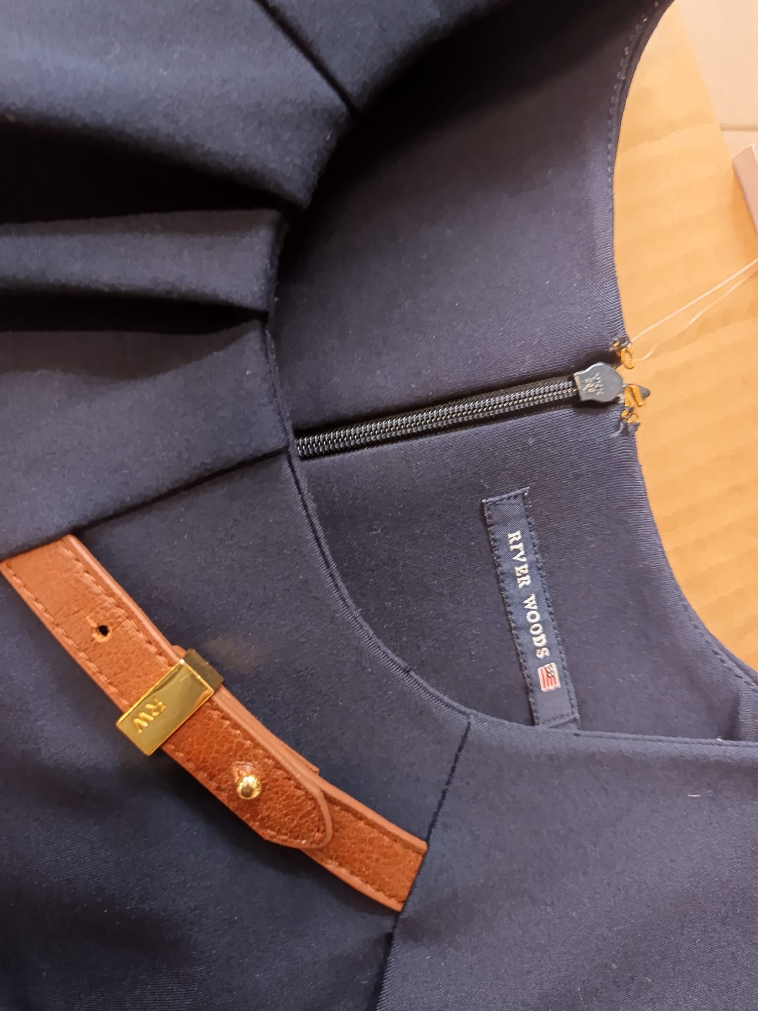 Granatowa sukienka z ozdobnym brązowym paskiem ze złotą klamrą i widocznym zamkiem błyskawicznym oraz metką River Woods.