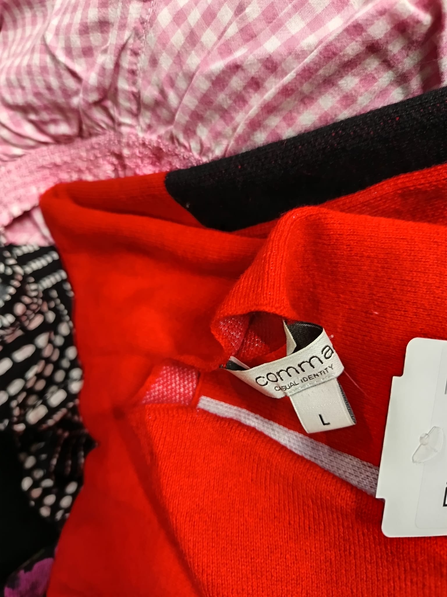 Stos ubrań: czerwony sweter z metką Comma w rozmiarze L, bluzka w różową kratkę gingham, czarny materiał i wzorzysta tkanina w kropki.