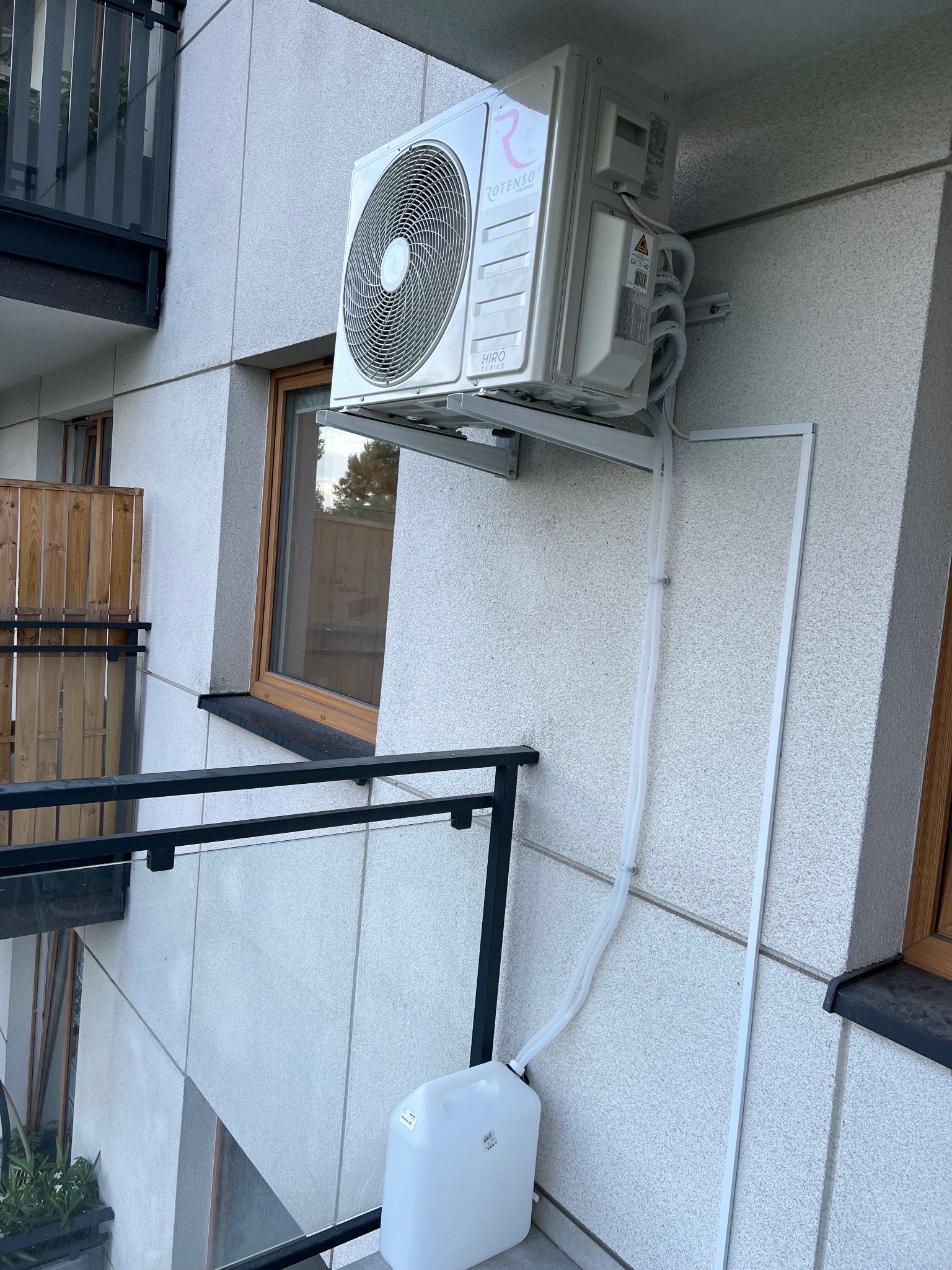 Klimatyzator Rotenso Hiro Series zamontowany na balkonie, z odprowadzeniem skroplin do kanistra. Widok z dołu, instalacja na elewacji budynku.