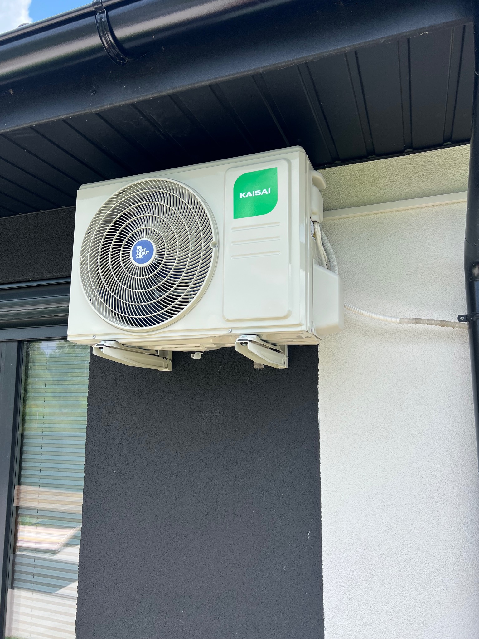 Zamontowana jednostka zewnętrzna klimatyzacji Kaisai na elewacji budynku z czarną rynną i fragmentem okna. Widoczne przewody i wsporniki montażowe.