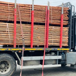 Tartak Amesko Spółka Jawna Monika Skóra-Szydłowska,Artur Szydłowski - Ciężarówka z załadowanym stosem tarcicy budowlanej zabezpieczonej czerwonymi pasami transportowymi, widoczne opony i błotniki pojazdu.