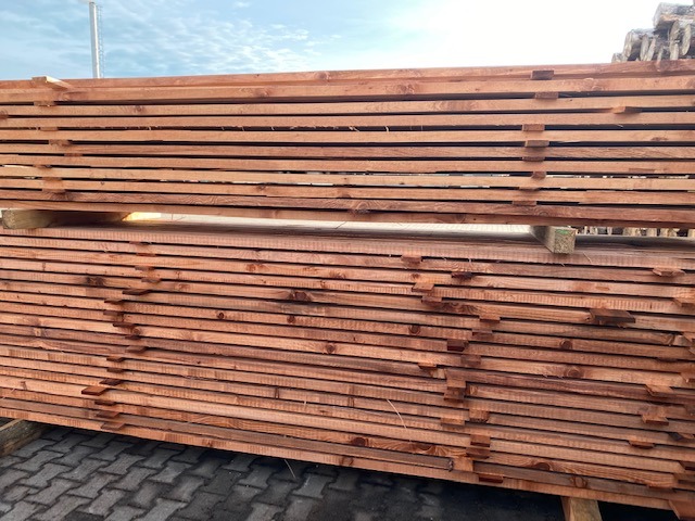 Ułożone w stosy deski tarcicy budowlanej z widocznym rysunkiem słojów, oddzielone przekładkami, gotowe do transportu.
