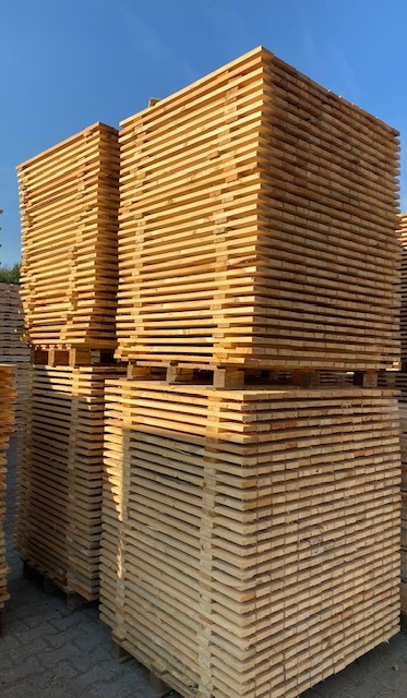 Stosy świeżo przetartego drewna ułożone na paletach, widoczne słoje i jasna barwa surowca.