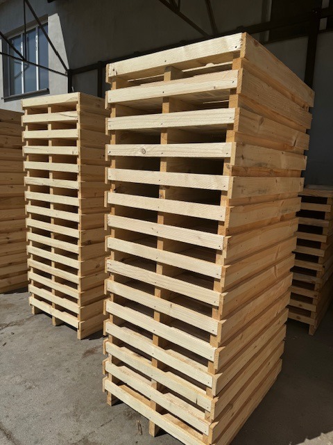 Stosy jasnej tarcicy budowlanej ułożone w wysokie konstrukcje w magazynie, widoczne ślady po obróbce drewna.