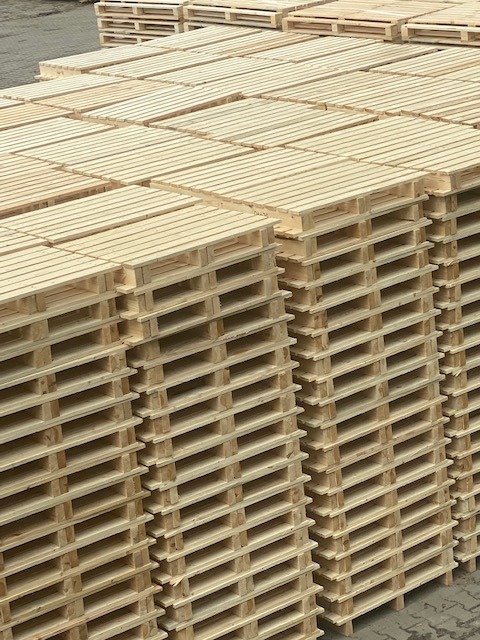 Stosy nowych, jasnych palet drewnianych ułożonych równo na zewnątrz, widoczne szare podłoże w tle.
