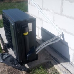 KlimaWentKomfort Mirosław Gawin - Czarna jednostka zewnętrzna pompy ciepła Seyva zamontowana przy ścianie budynku z betonu komórkowego, z widocznymi przewodami w peszlach.