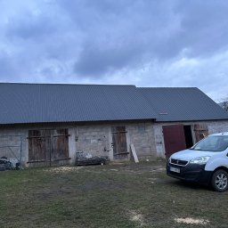 Usługi dekarskie - Budynek gospodarczy z nowym, szarym dachem z blachy trapezowej, zaparkowany biały bus dostawczy, pochmurne niebo.