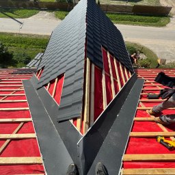 Usługi dekarskie - Montaż obróbek blacharskich na dachu z czerwoną membraną, widok z góry na fragment dachu z częściowo ułożonym pokryciem w kolorze grafitowym.