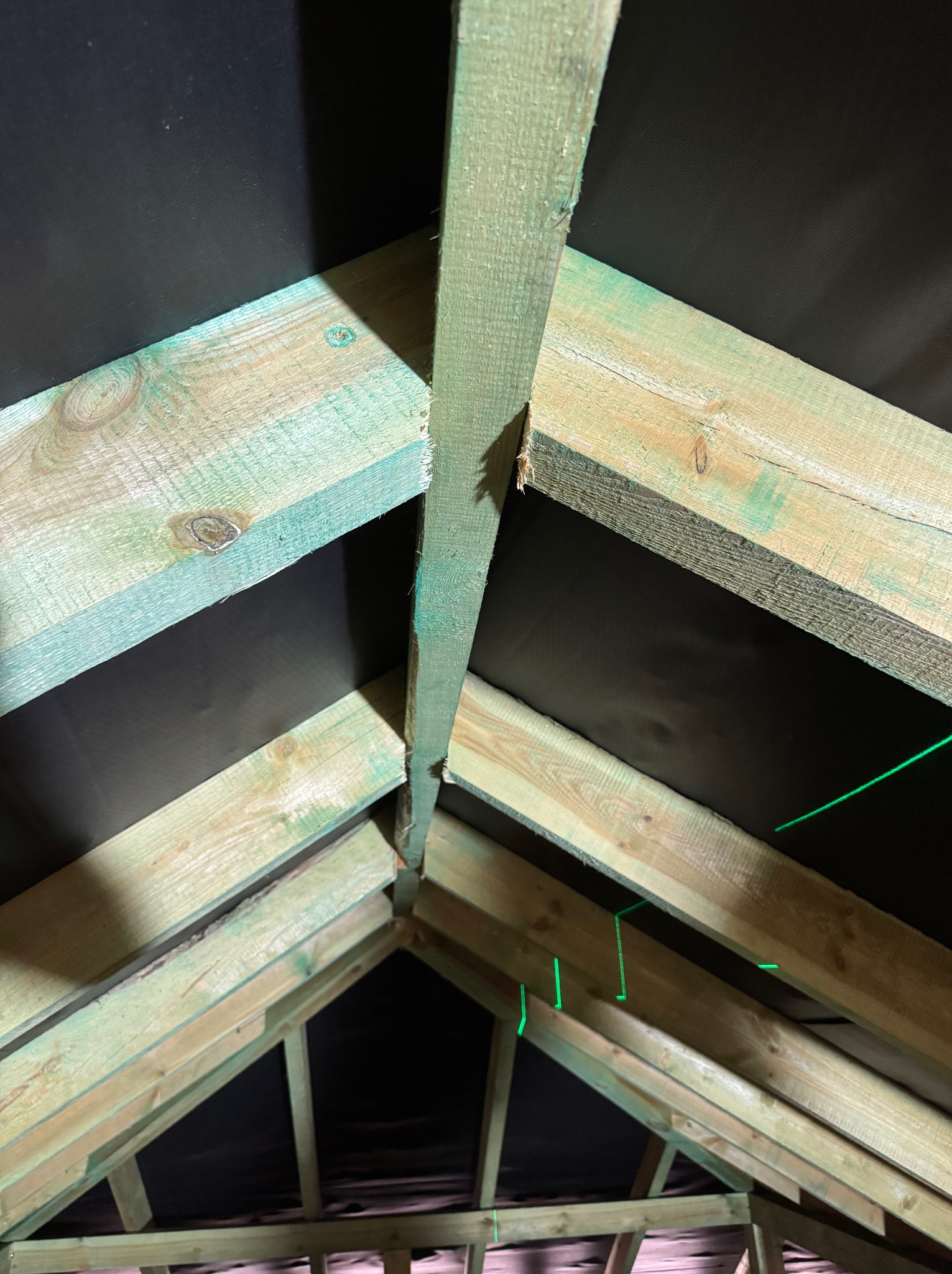 Drewniana konstrukcja dachu od wewnątrz, z widoczną membraną dachową i zielonymi elementami impregnacji. Ujęcie z dołu, ukazujące detale łączeń i strukturę drewna.