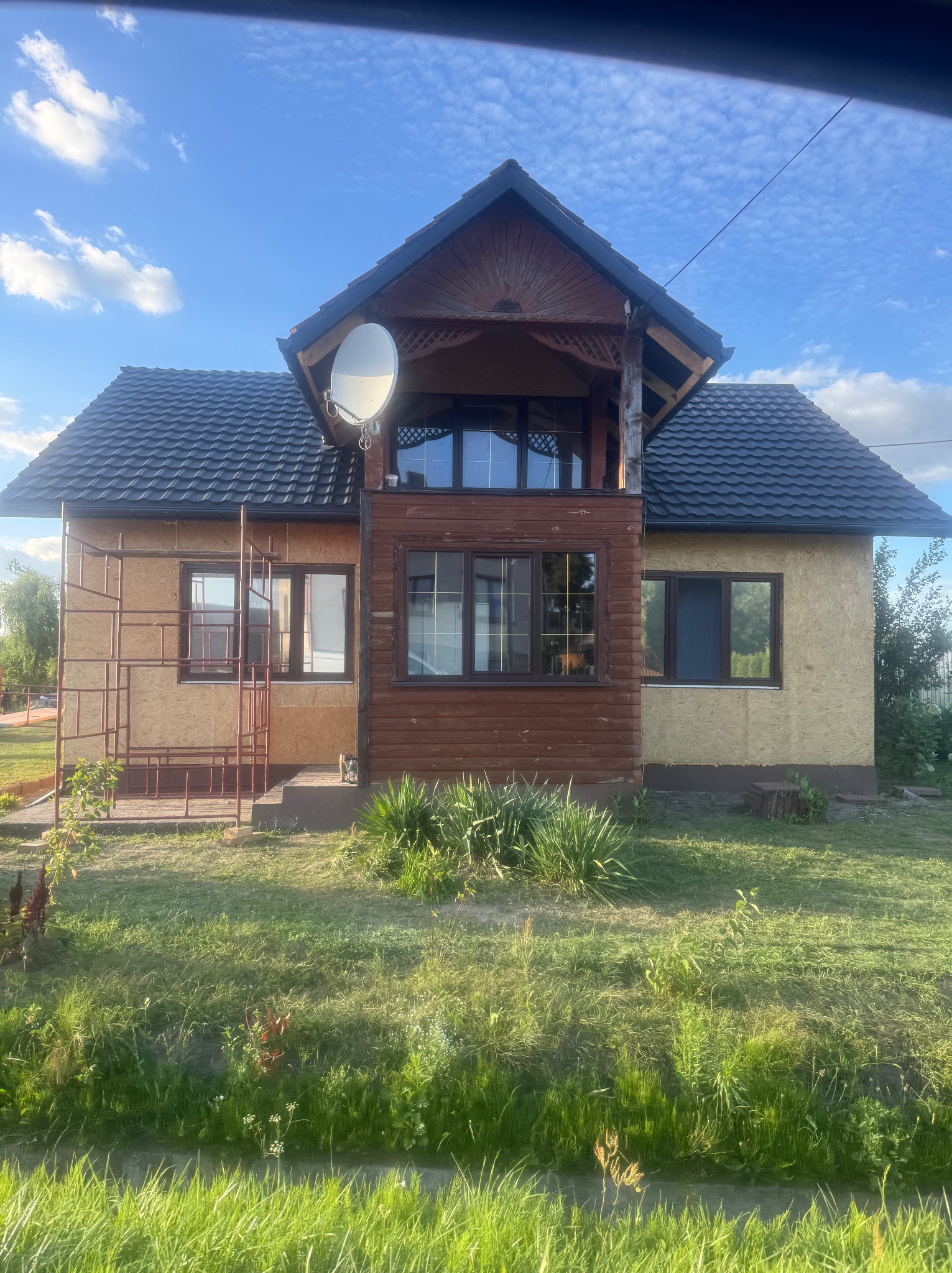 Dom w trakcie prac wykończeniowych elewacji, z widocznym rusztowaniem i nowym, ciemnym dachem. Na dachu zamontowana antena satelitarna.