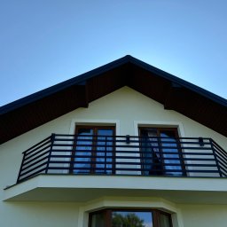 WELD- MET Tomasz Dziadykiewicz - Czarna, pozioma balustrada balkonowa z metalowych profili na tle białej elewacji domu z brązowym dachem i błękitnego nieba.