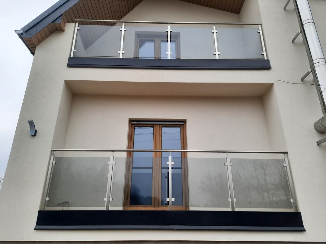 Dwa balkony z balustradami szklanymi na budynku w Nowej Wsi. Balustrady ze stali nierdzewnej z szybami, czarne elementy wykończeniowe.
