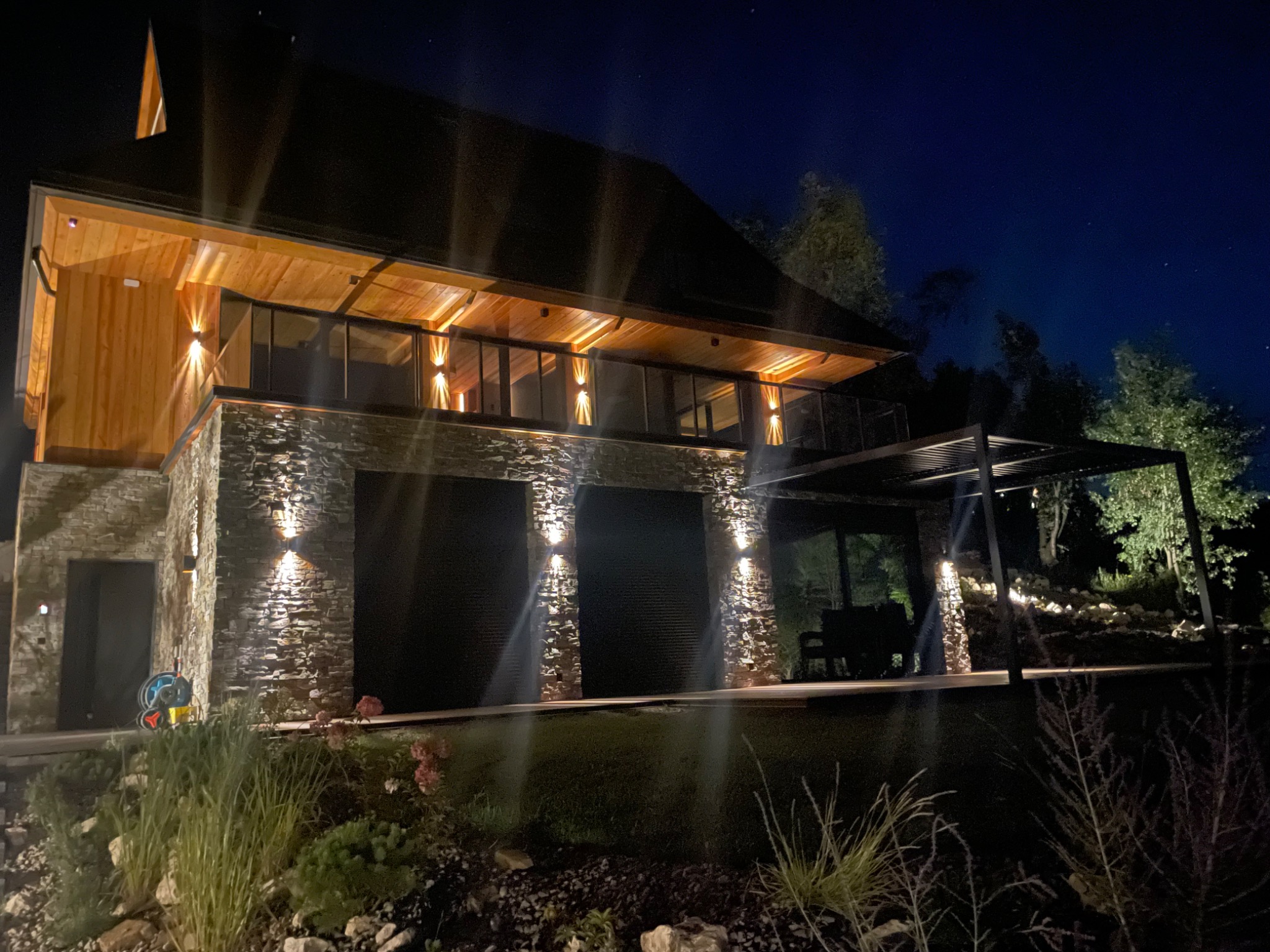 Dwukondygnacyjny dom z kamienną elewacją i drewnianym wykończeniem, oświetlony zewnętrznymi lampami ściennymi, nocą.