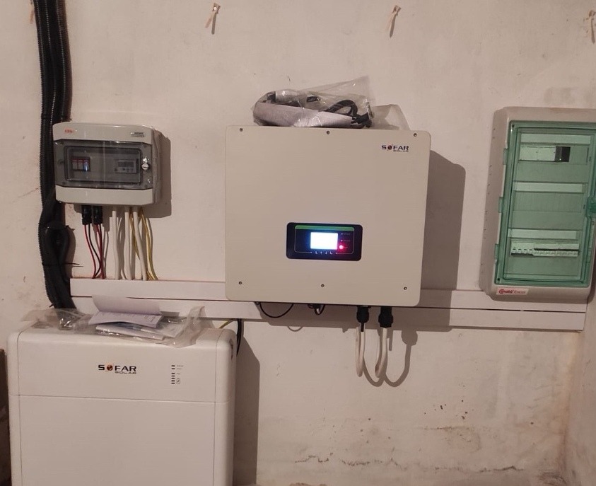 Zamontowany inwerter fotowoltaiczny SOFAR wraz z akumulatorem i rozdzielnicami elektrycznymi na ścianie z widocznymi zaciekami.