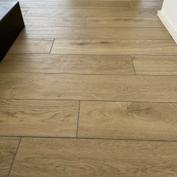 Usługi budowlane płytki - Ułożona podłoga z płytek imitujących drewno, widoczne fugi i fragment ściany z listwą przypodłogową.