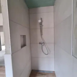 Płytki ścienne w odcieniach beżu ułożone poziomo w kabinie prysznicowej z wnęką w ścianie, widoczna armatura i odpływ liniowy w podłodze z płytek imitujących drewno, sufit wykończony płytą...