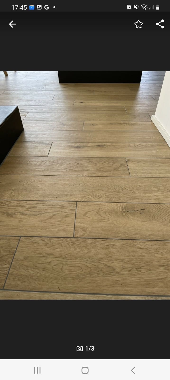 Ułożona podłoga z płytek imitujących drewno, widoczne fugi i fragment ściany z listwą przypodłogową.