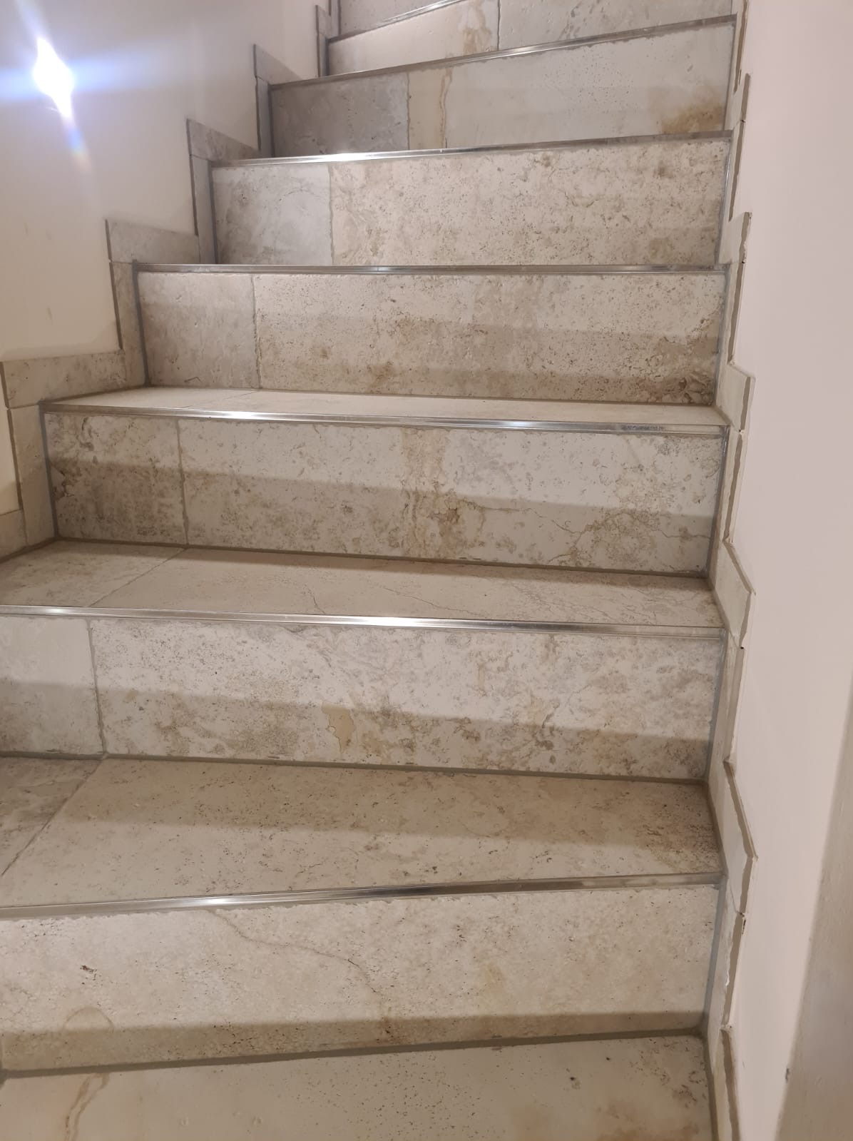 Schody wyłożone płytkami imitującymi marmur, z metalowymi listwami na krawędziach stopni, widok z góry.