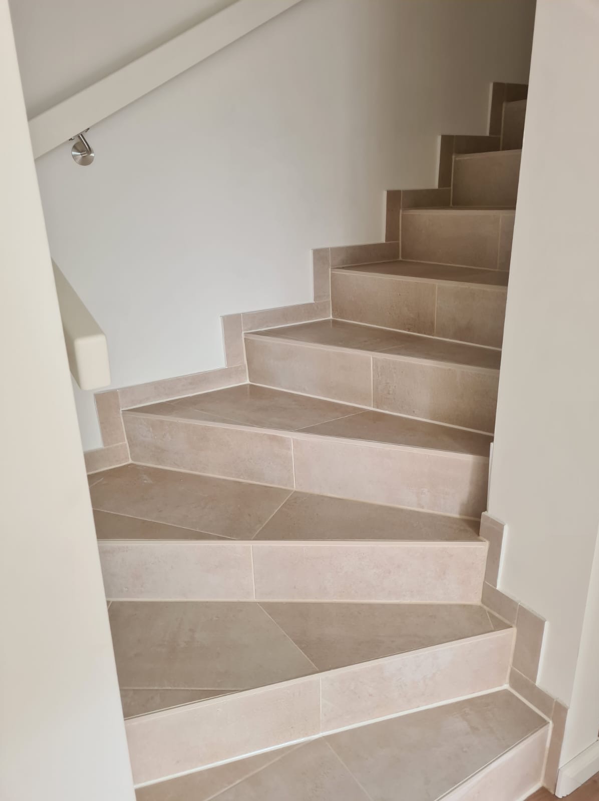 Schody wyłożone beżowymi płytkami ceramicznymi w jasnym wnętrzu, widok z dołu, z delikatnym oświetleniem.