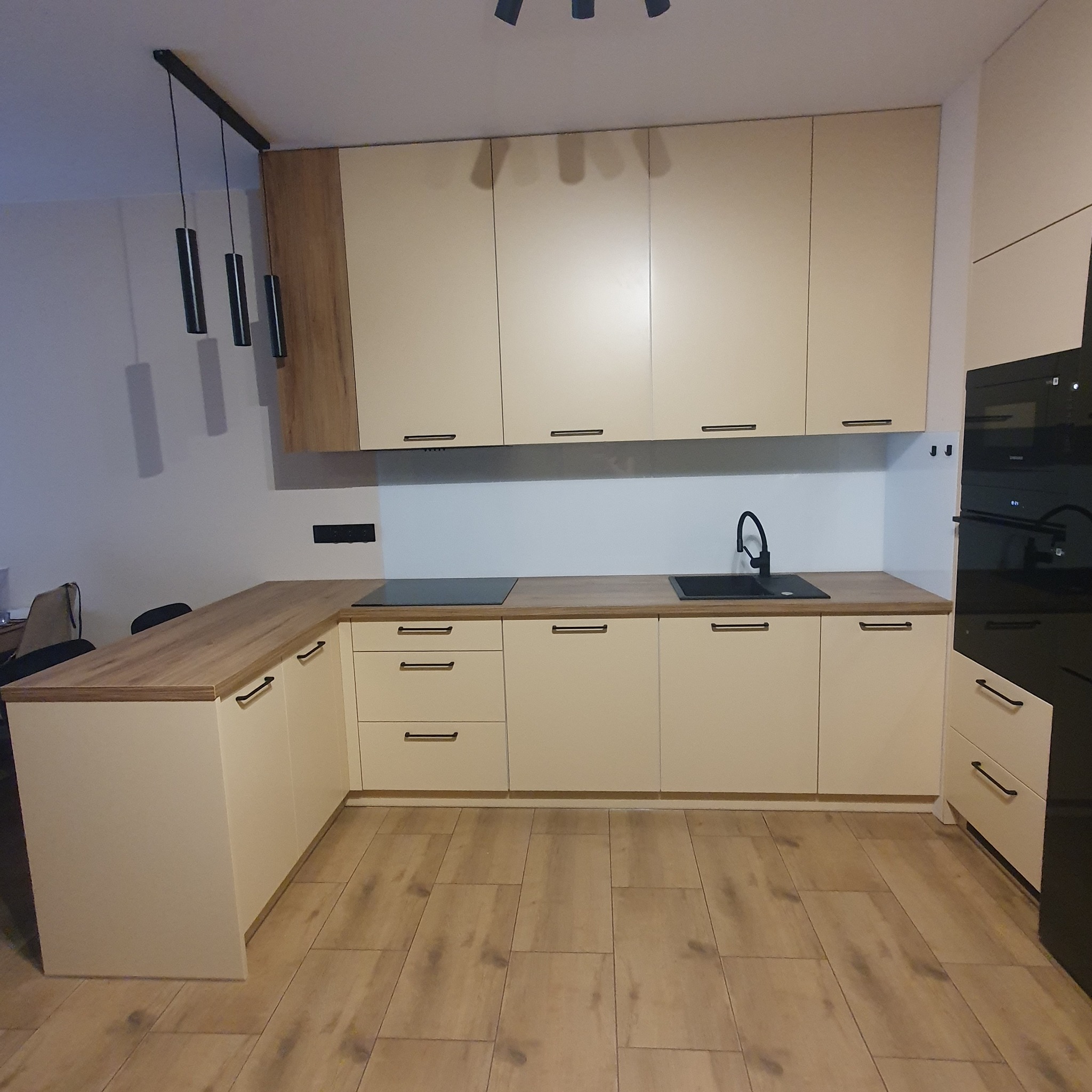 Jasna kuchnia na wymiar z drewnianym blatem i czarną armaturą, widziana w Łopienniku Dolnym-Kolonii, oświetlona nowoczesnymi lampami wiszącymi.