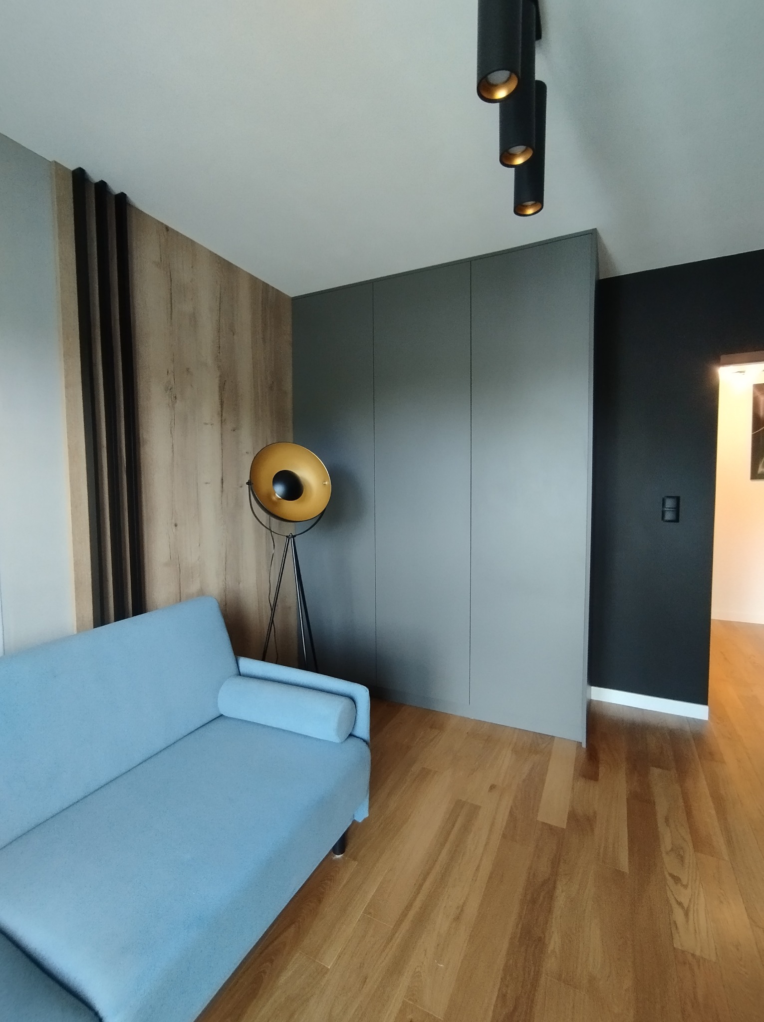 Nowoczesny salon z błękitną sofą, szarą szafą w zabudowie, drewnianą ścianą dekoracyjną, lampą podłogową w stylu retro i parkietem w odcieniach miodu.