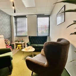 Dobry Psycholog - Klimatyczny gabinet z zielonymi fotelami i kanapą, stolikiem z zabawkami dla dzieci, jasnymi ścianami i dużymi oknami z żaluzjami.