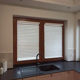 Kuchnia z oknem wyposażonym w poziome, białe listewki regulujące dopływ światła, widoczny zlew i czarna bateria.