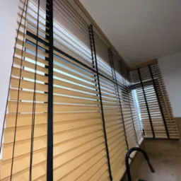 Jasne, drewniane lamele z czarnymi taśmami w oknie, widok z dołu, fragment zlewu na pierwszym planie.