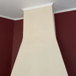 Wykończony fragment ściany z dekoracyjną strukturą i białym gzymsem, sąsiadujący z pomalowaną na bordowo ścianą. Widok z dołu.