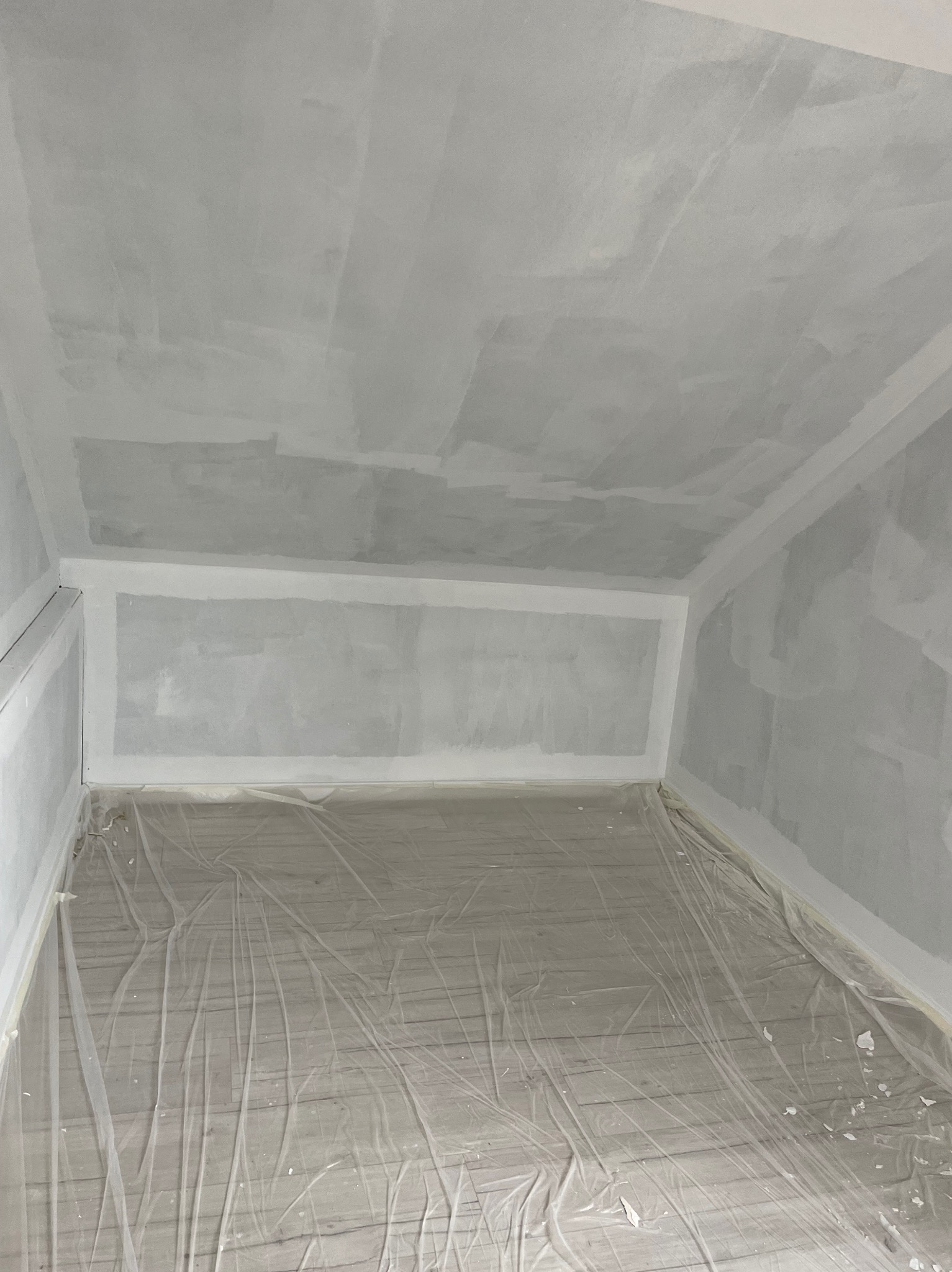 Pokój w trakcie prac przygotowawczych do malowania, ściany i sufit wstępnie wyszpachlowane, podłoga zabezpieczona folią ochronną.