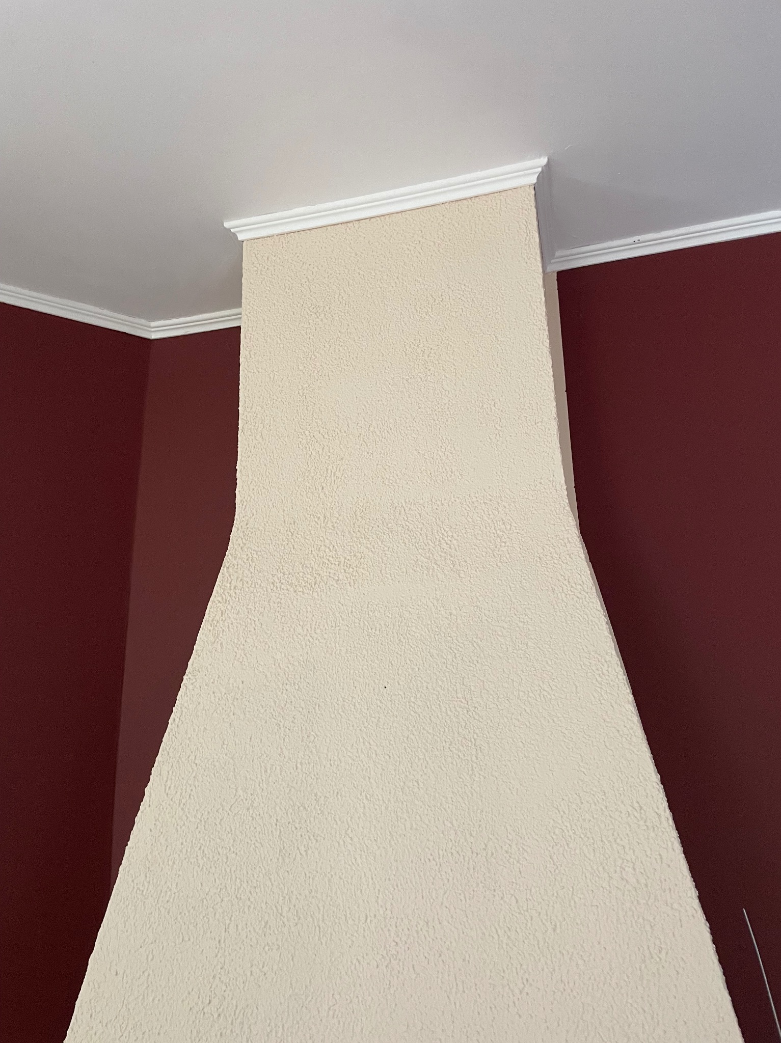 Wykończony fragment ściany z dekoracyjną strukturą i białym gzymsem, sąsiadujący z pomalowaną na bordowo ścianą. Widok z dołu.