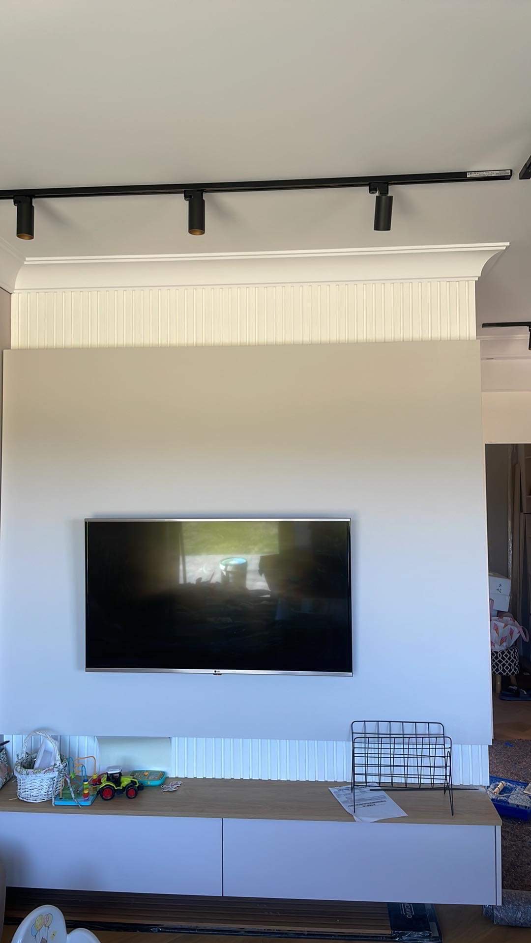 Ściana salonu po remoncie z zamontowanym telewizorem, oświetleniem szynowym i dekoracyjną boazerią panelową nad i pod szafką RTV.