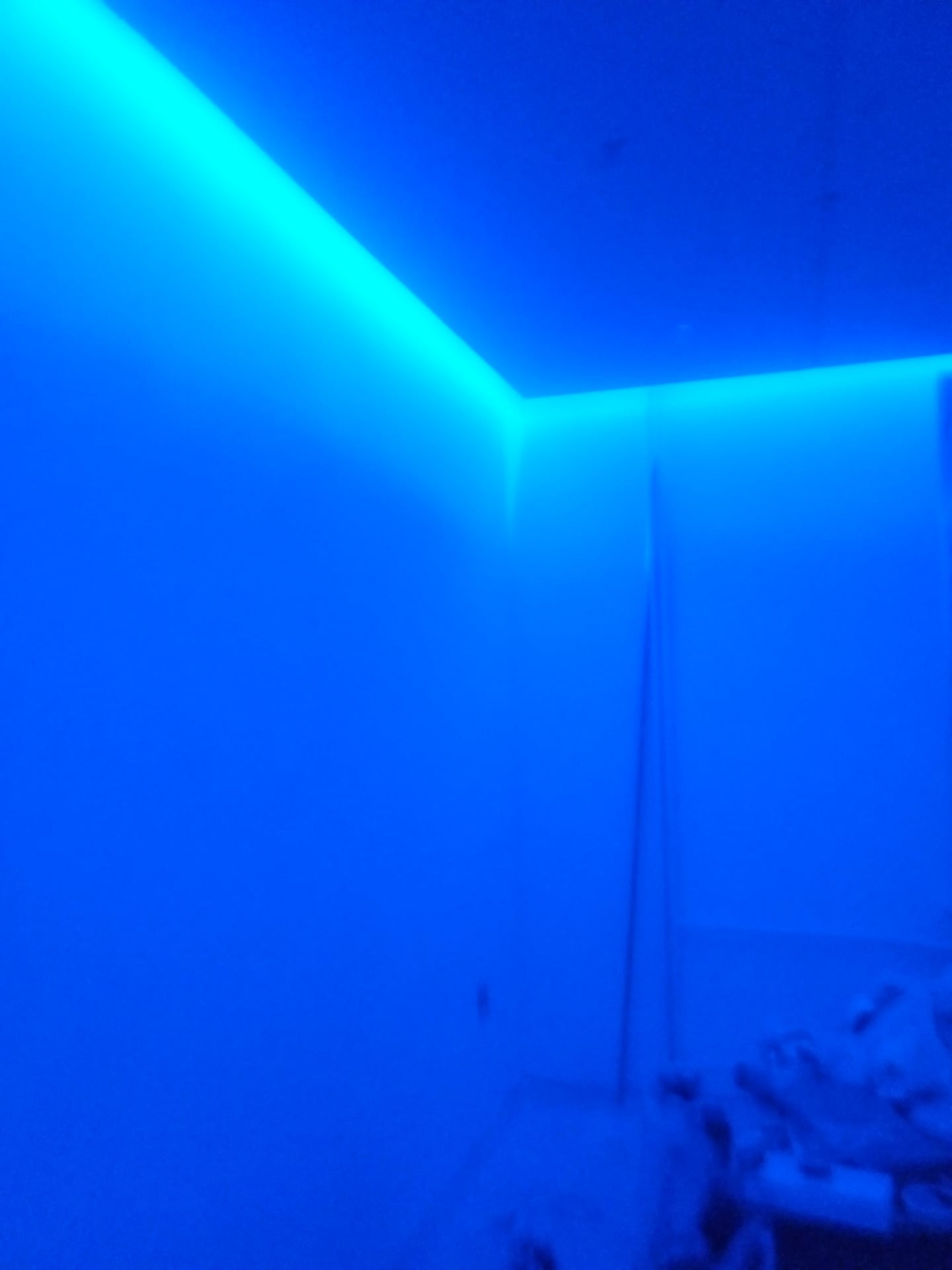 Niebieskie oświetlenie LED zamontowane wzdłuż sufitu i ściany, tworzące nowoczesny efekt wizualny w pokoju o białych ścianach.