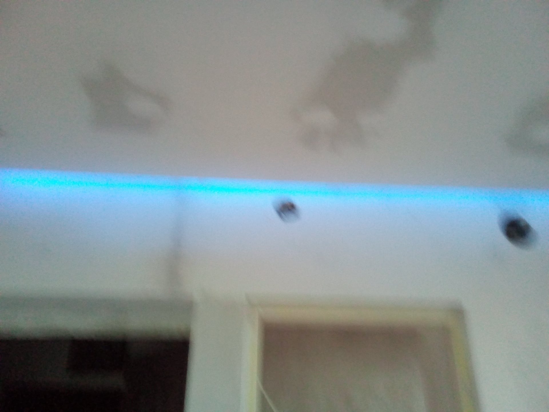 Niejasne ujęcie sufitu z niebieskim oświetleniem LED w Bielsko-Białej, widoczne plamy i otwory na oświetlenie punktowe.