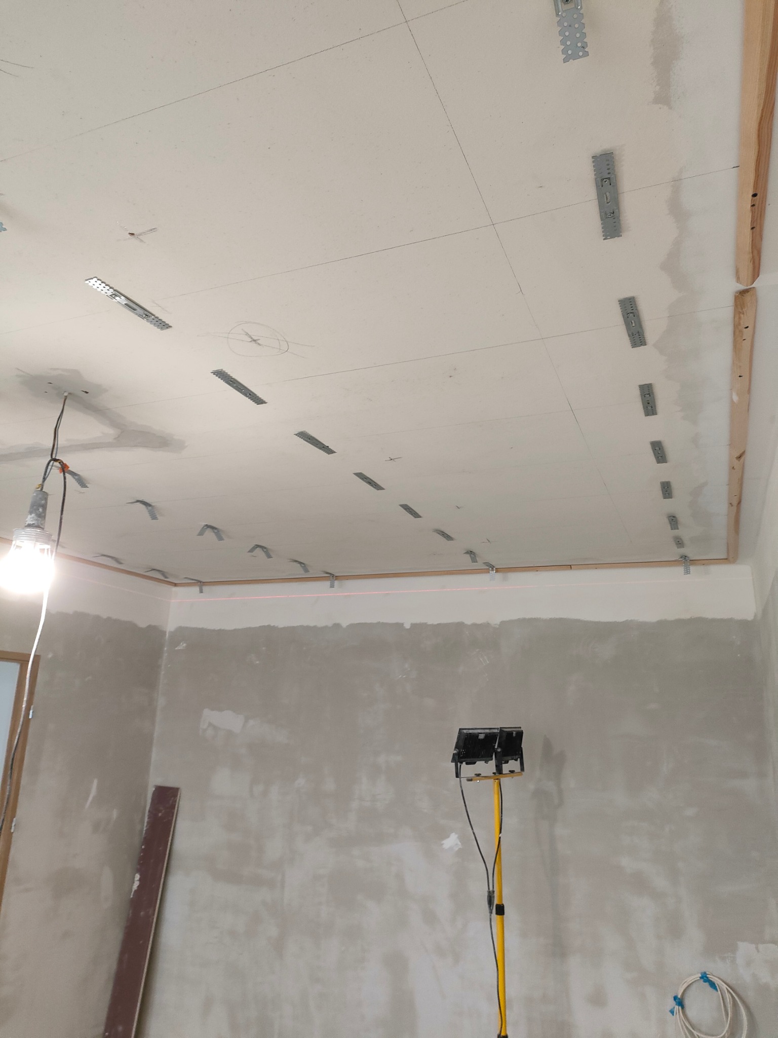 Montaż stelaża pod płytę gipsowo-kartonową na suficie w trakcie prac w Bielsku-Białej, widoczny laserowy poziom, metalowe profile i drewniane elementy konstrukcyjne.