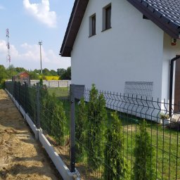 ARTPRO OGRODZENIA - Nowoczesne ogrodzenie panelowe z podmurówką betonową, obsadzone tujami, na tle domu z brązową dachówką i zielenią