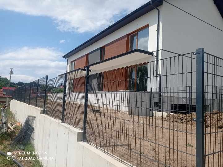 Nowoczesny dom jednorodzinny z czarnym ogrodzeniem panelowym na betonowej podmurówce, widok z dołu w słoneczny dzień.