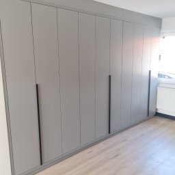 MEBLE-SKIBA TOMASZ SKIBA - Szara szafa wnękowa z długimi, czarnymi uchwytami, dopasowana do sufitu, na podłodze panele imitujące jasne drewno, widok z dołu.