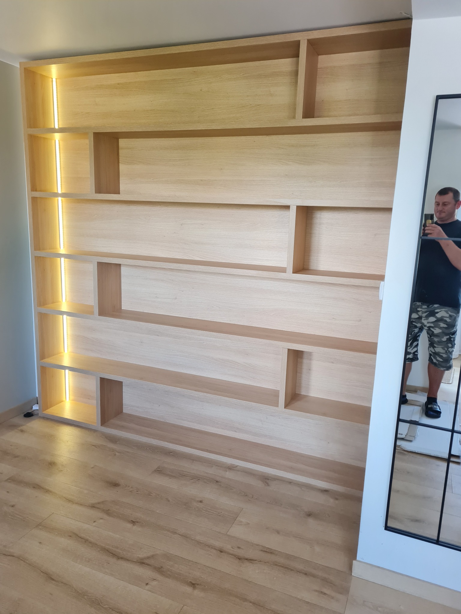 Drewniana szafa na wymiar z wbudowanym oświetleniem LED, widoczna w lustrze osoba robiąca zdjęcie.