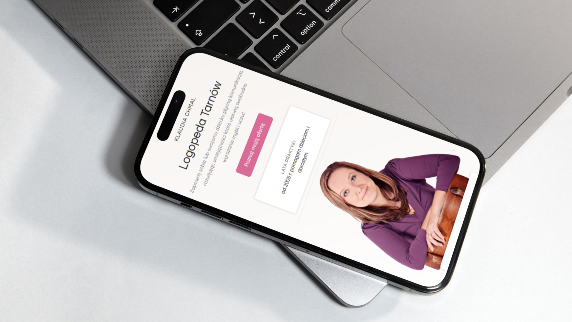 Smartfon wyświetlający stronę internetową logopedy Klaudii Chmal, leżący na laptopie. Widoczny tekst o zapewnieniu płynnej komunikacji i zdjęcie logopedy.