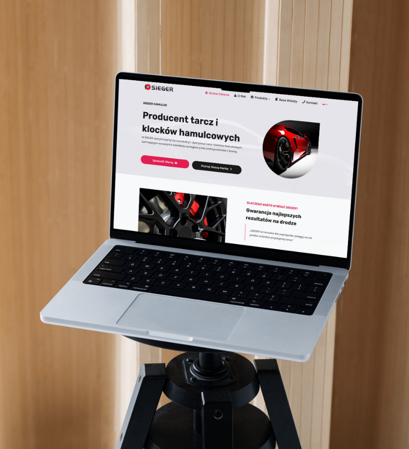 Laptop na czarnym statywie prezentuje stronę internetową producenta tarcz i klocków hamulcowych Sieger, z czerwonym sportowym autem w tle.