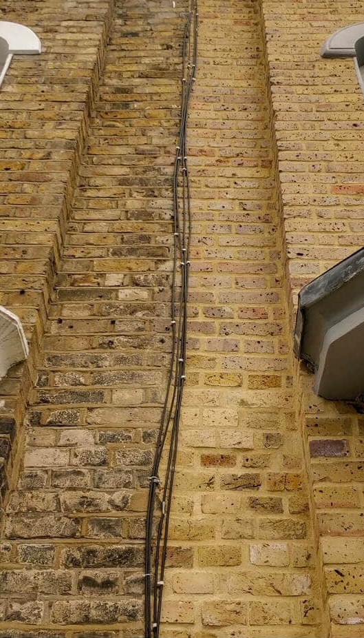 Elewacja budynku z żółtej cegły z widocznymi kablami przymocowanymi do ściany za pomocą białych uchwytów.