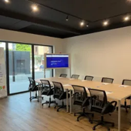 Sala szkoleniowa z długim stołem, krzesłami i ekranem prezentującym kompleksowe usługi pomiarowe, widoczny baner firmy Husdromo z ofertą BHP i adres firmy.