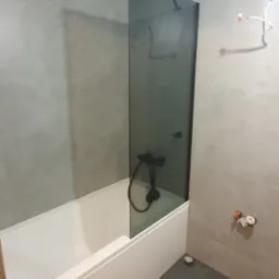 Nowoczesna łazienka z szarymi płytkami, białą wanną i czarną armaturą. Kabina prysznicowa z ciemnego szkła. Minimalistyczny design.