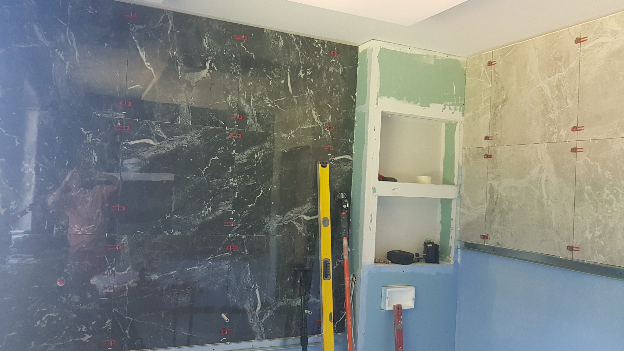 Montaż płytek imitujących marmur na ścianie w Malborku, widoczne poziomice i akcesoria glazurnicze, wnęka z płyt karton gips.