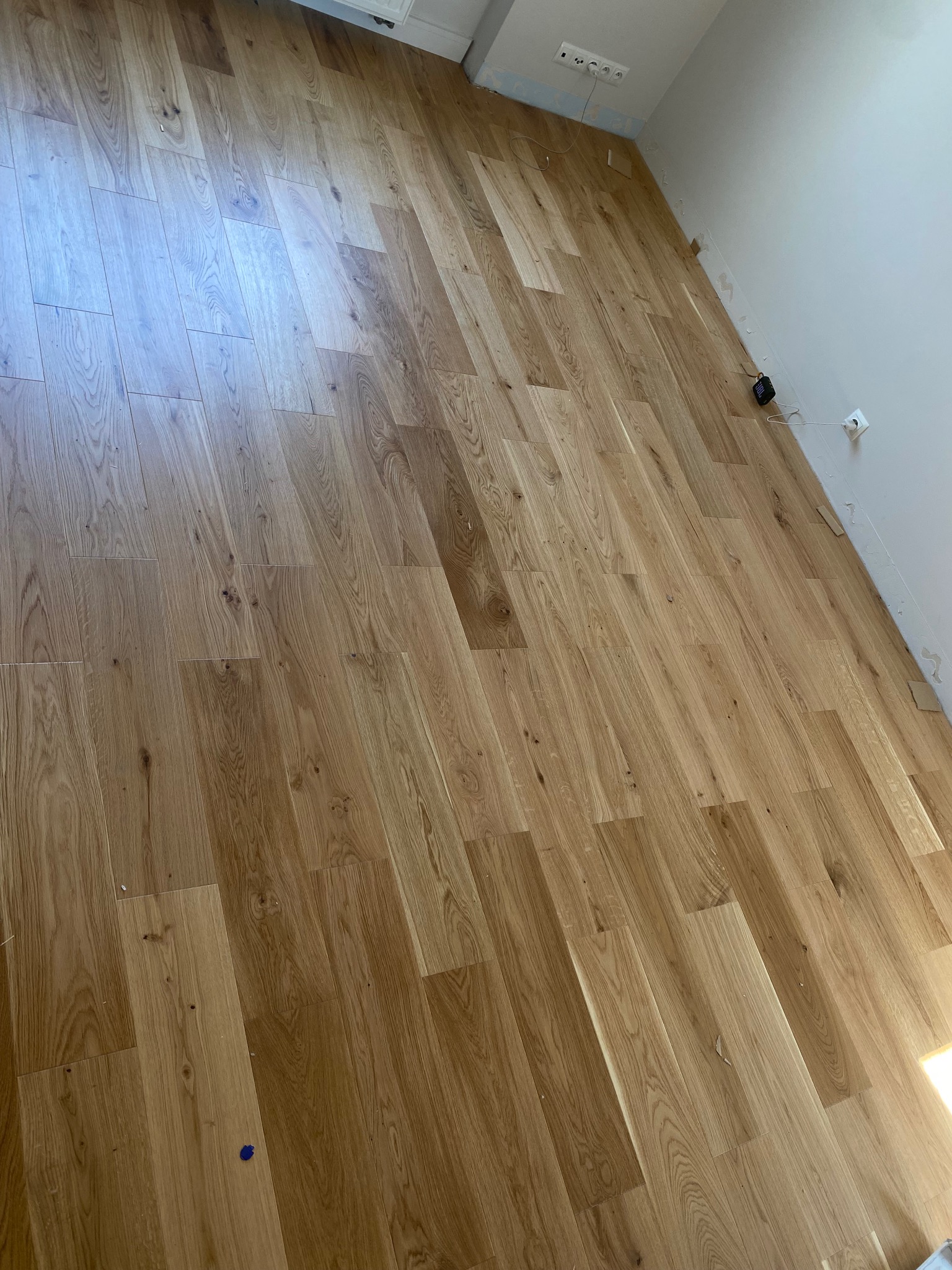 Ukończona podłoga z paneli drewnopodobnych w jasnym odcieniu, widoczne niedociągnięcia w wykończeniu przy ścianach i gniazdkach elektrycznych.