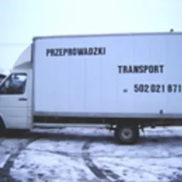Biały samochód dostawczy z napisem 'PRZEPROWADZKI TRANSPORT 502 021 871' zaparkowany na śniegu, widoczne ślady opon.