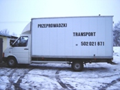Biały samochód dostawczy z napisem 'PRZEPROWADZKI TRANSPORT 502 021 871' zaparkowany na śniegu, widoczne ślady opon.