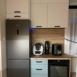 MasrockMeble - Nowoczesna kuchnia z zabudową: białe szafki górne, lodówka Hotpoint Ariston, błękitne szafki dolne z piekarnikiem Electrolux, drewniany blat i sprzęty AGD na blacie.